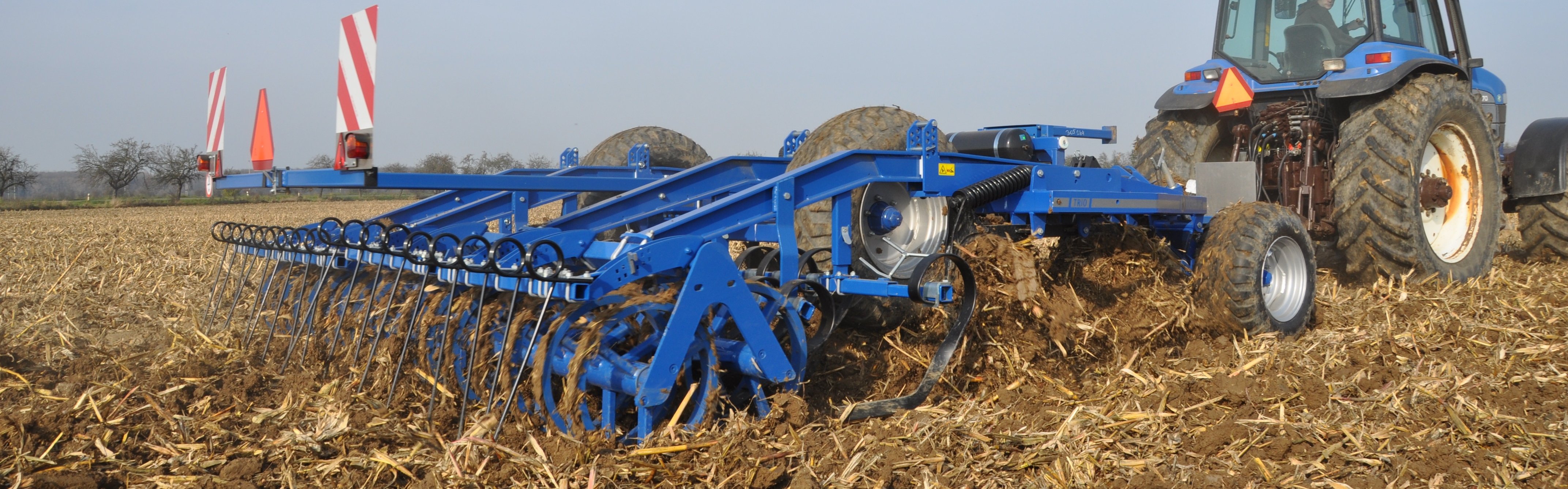 Modrý třířadý podmítač s integrovaným podvozkem s traktorem na poli