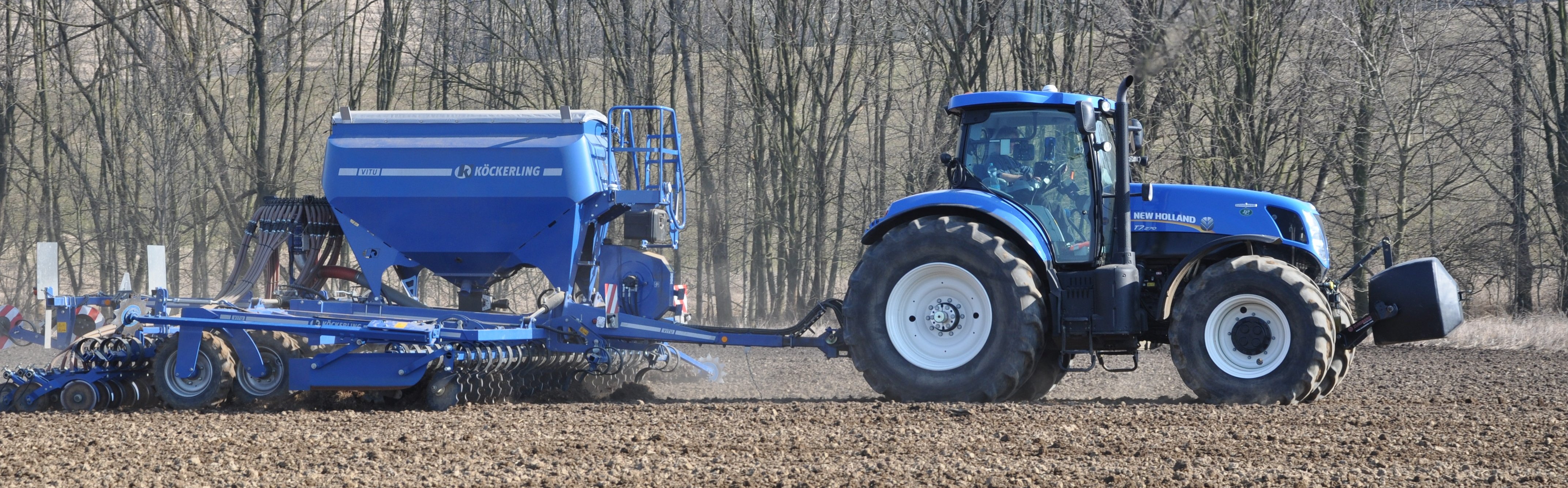Kombinovaný secí stroj s modrým traktorem na poli