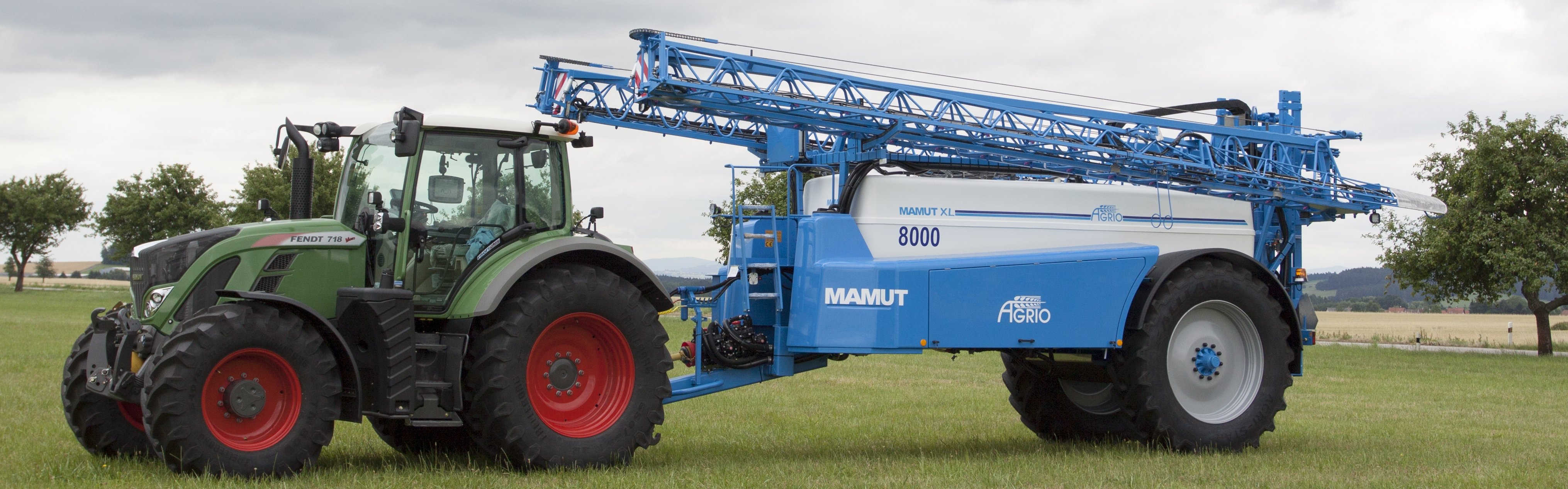 Modrý tažený postřikovač a zelený traktor na poli